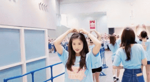 a girl in a blue shirt is making a heart with her hands in front of a crowd .
