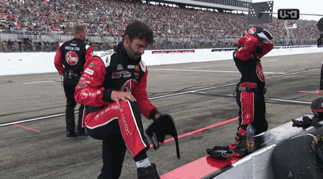 a race car driver is kneeling down on the side of a race track