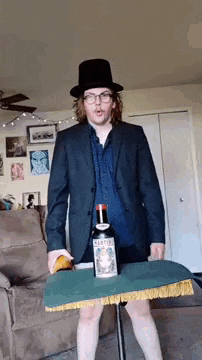 a man in a suit and top hat is standing next to a bottle of martini .