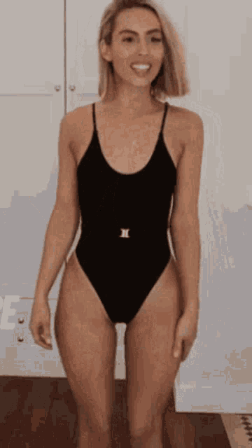 a woman in a black swimsuit is standing on a wooden floor .