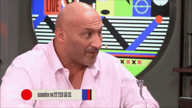 a bald man in a pink shirt is sitting in front of a screen that says live