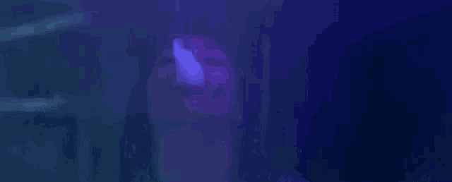 a close up of a person smoking a cigarette in a dark room with a purple light coming out of their mouth .