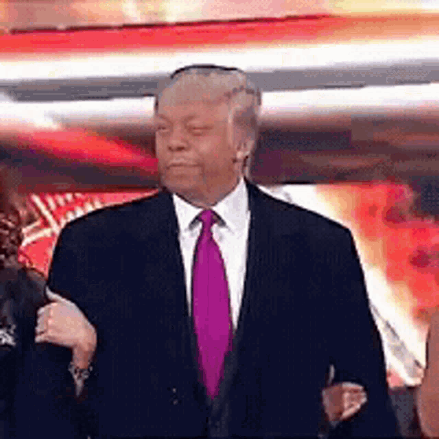 a man in a suit and tie is giving a thumbs up while standing on a stage .