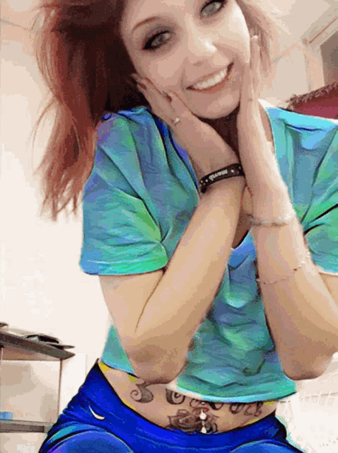 a woman wearing a tie dye shirt and blue shorts has a tattoo on her belly
