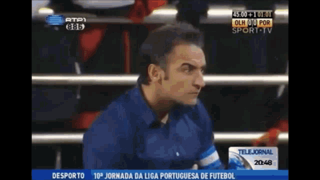 a man in a blue shirt is sitting in front of a screen that says telejornal