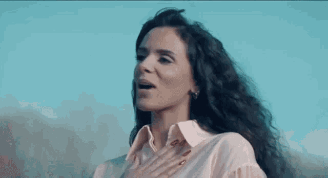 a woman with long curly hair is singing into a microphone while standing in front of a blue sky .