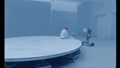 a man in a red hat sits on a round table in a dark room
