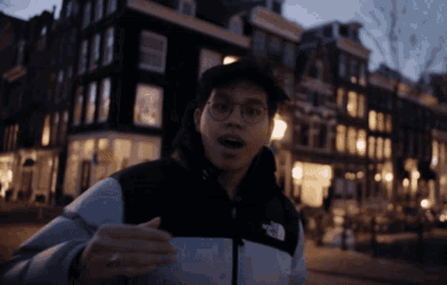 a man wearing a north face jacket stands in front of buildings