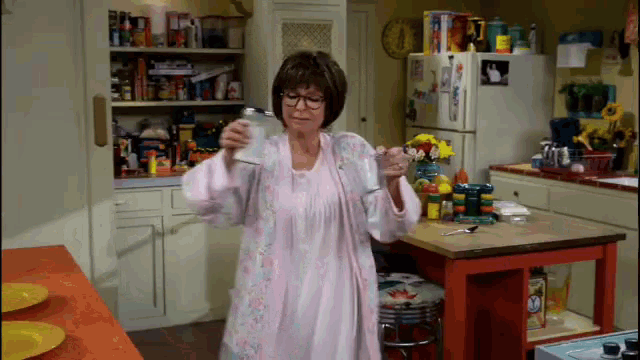 a woman in a pink robe is standing in a kitchen drinking from a can