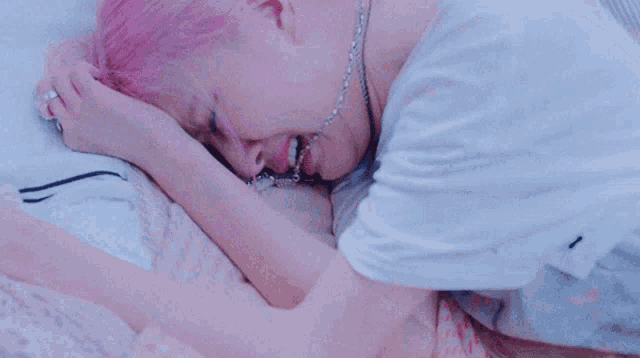 a woman with pink hair is laying on a bed with a necklace around her neck .
