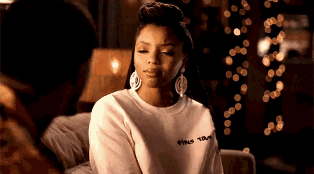 a woman is sitting on a couch with her eyes closed and wearing a white sweatshirt .