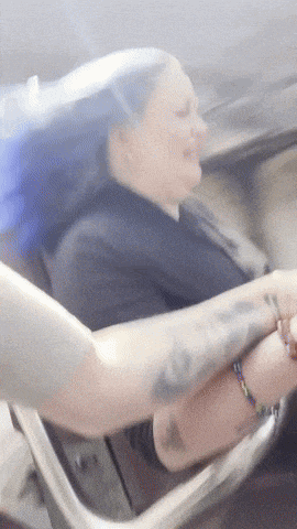a woman with a tattoo on her arm sits in a chair with her hair blowing in the wind