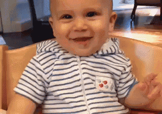 a baby in a striped shirt is sitting in a high chair smiling .