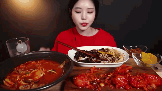 a woman in a red sweater is eating a plate of food with chopsticks