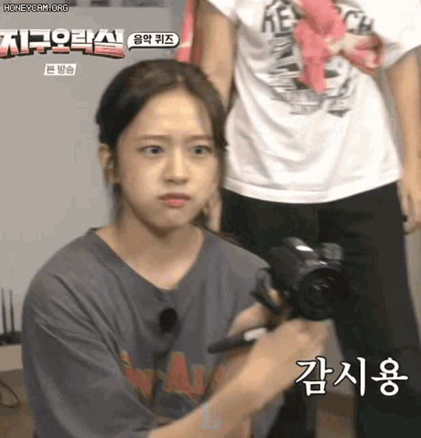 a girl is holding a camera with korean writing on the bottom