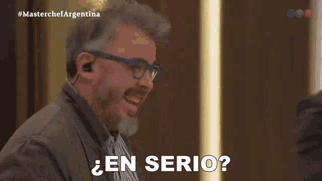 a man with glasses and a beard is laughing in front of a screen that says masterchefargentina