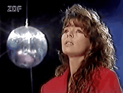 a woman in a red jacket stands in front of a disco ball with zdf written on the bottom right