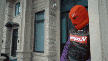 a man wearing an orange ski mask is standing in front of a large brick building