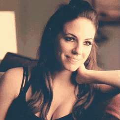 a woman in a black tank top is smiling with her hand on her face