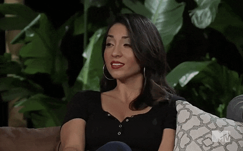 a woman in a black shirt is sitting on a couch with a plant in the background .