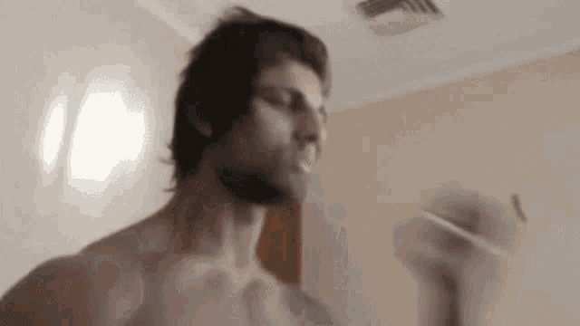 a shirtless man is standing in a room with his arms outstretched in a blurry photo .