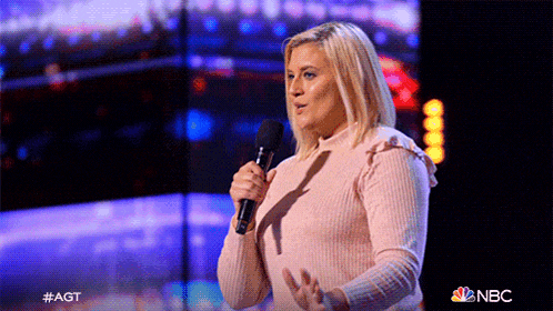 a woman in a pink sweater is holding a microphone in front of a screen that says nbc on it