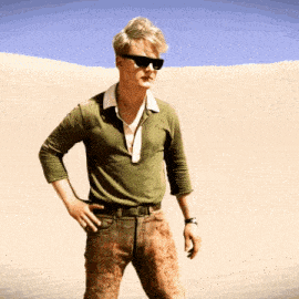 a man wearing sunglasses and a green shirt is standing in the sand