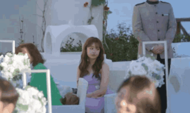 a woman in a purple dress is sitting in front of a white building