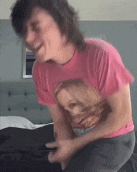 a man wearing a pink shirt with a picture of a woman on it is sitting on a bed