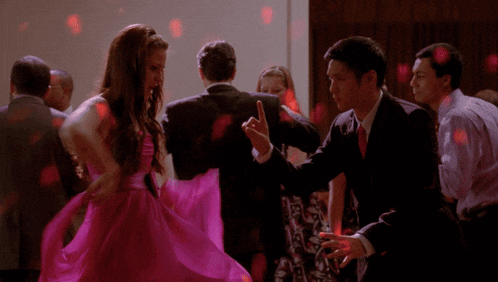 a woman in a pink dress is dancing next to a man in a suit