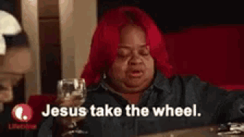 a woman with red hair is sitting at a table holding a glass of wine and says jesus take the wheel .