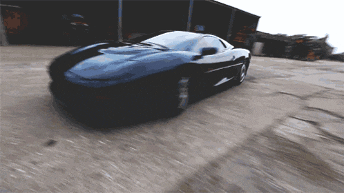 a black sports car is driving down a dirt road in front of a building