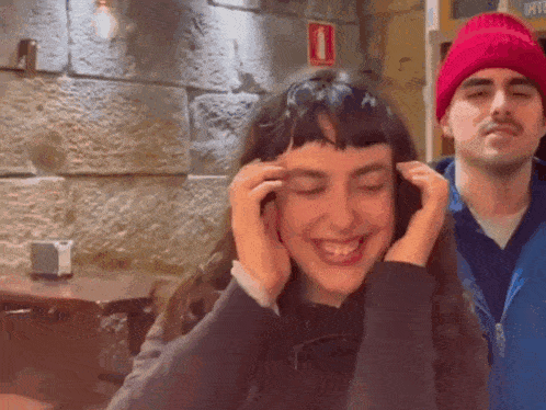 a woman wearing headphones is smiling while standing next to a man wearing a red beanie .