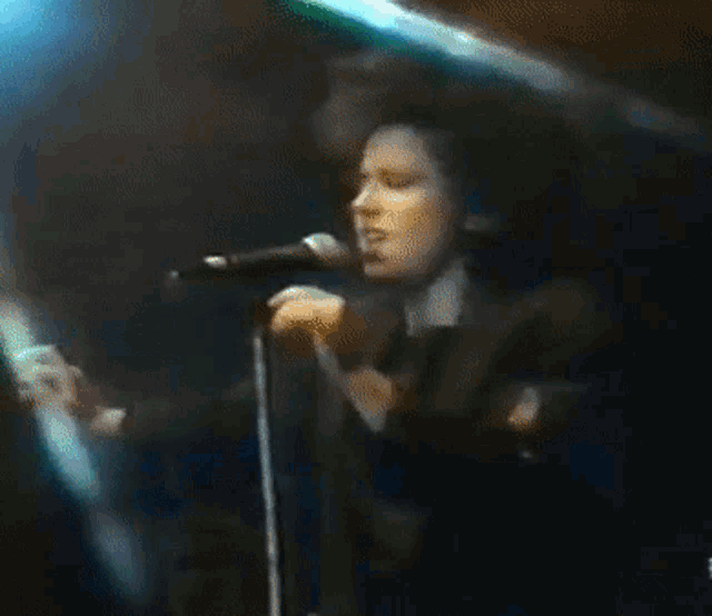 a man singing into a microphone with his hands up in the air