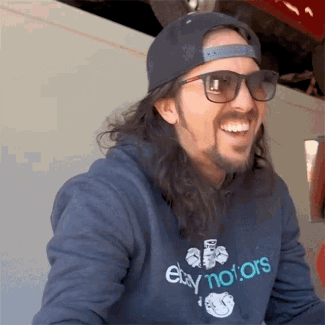 a man wearing sunglasses and a ebay motors sweatshirt smiles