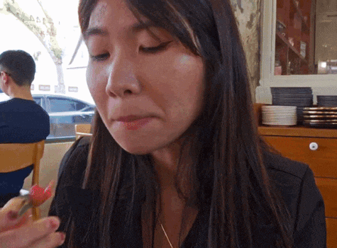 a woman with long dark hair is eating a piece of food with a fork