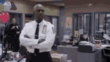 a police officer is standing in an office with his arms crossed and balloons in the background .