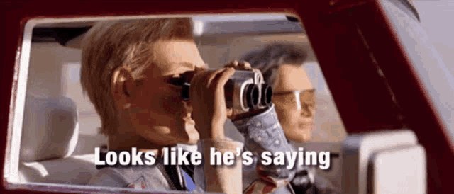 a man looking through binoculars in a car with the words looks like he 's saying next to him