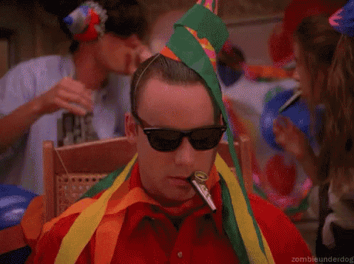 a man wearing sunglasses and a party hat is smoking a cigarette .