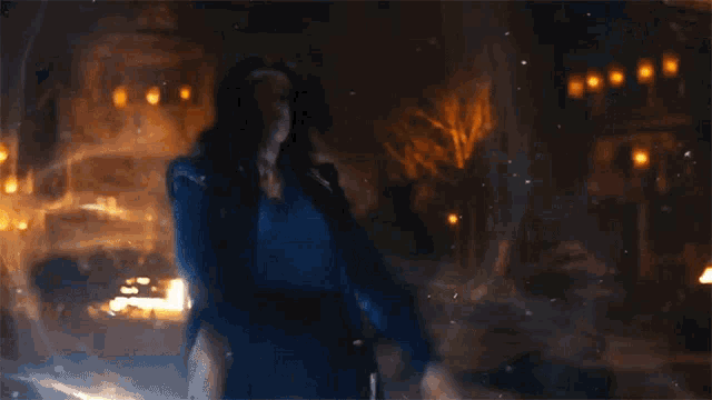 a person in a blue jacket is standing in front of a large fire .