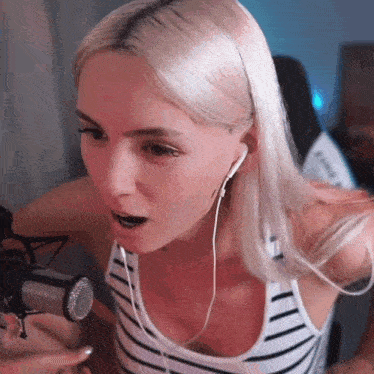 a blonde woman wearing headphones and a striped tank top is talking into a microphone .