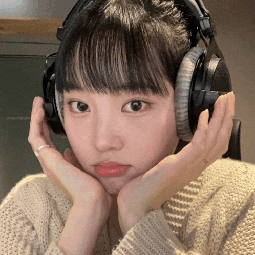 a woman wearing headphones looks at the camera with her hands on her face