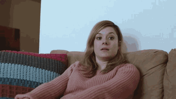 a woman in a pink sweater is sitting on a brown couch
