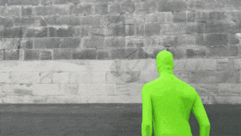 a man in a green hoodie is walking in front of a brick wall