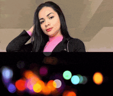 a woman in a pink top and black jacket is standing in front of a blurry background