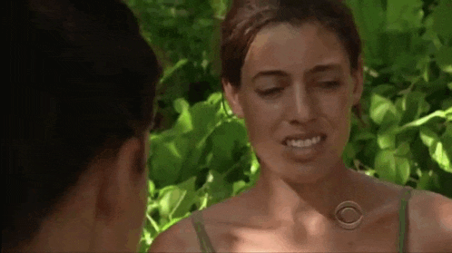 two women are standing next to each other in the woods and smiling .