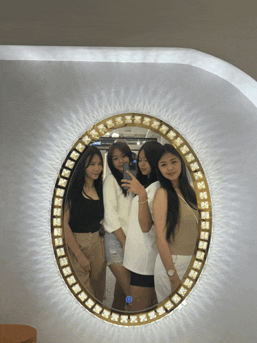 a group of girls are posing for a picture in front of a mirror that says ' selfie ' on it