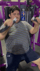 a man in a striped shirt and under armour shorts is using a machine at a gym