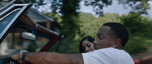 a man in a white shirt is driving a red convertible car