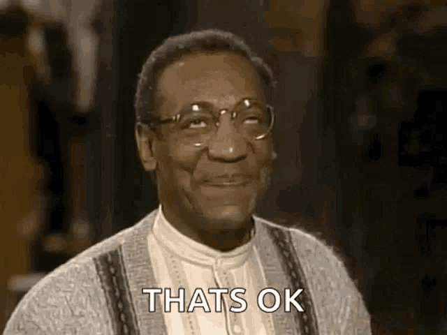 a man wearing glasses and a sweater is smiling and saying that 's ok .